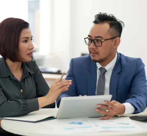 asian-man-woman-business-attire-sitting-indoors-with-tablet-talking